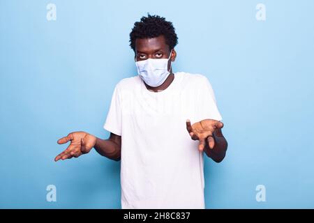Clueless man with face mask raising shoulders in confusion. Person with confused expression looking at camera while feeling unsure. Adult with coronavirus protection being uncertain Stock Photo
