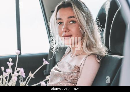 Young blonde girl sitting in the back seat of the car with flowers in defocus Stock Photo