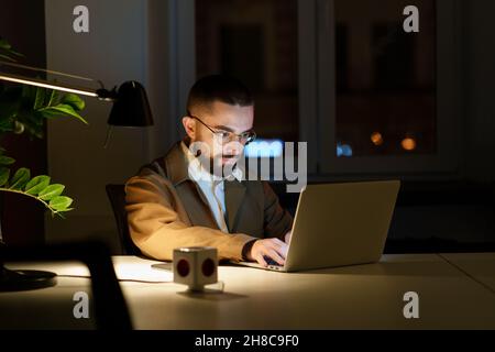 Concentrated programmer man work on laptop in evening in empty office o fixing bug in application Stock Photo