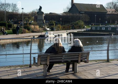 Two women sat on a bench overlooking Bancroft Gardens canal basin, Stratford-upon-Avon, Warwickshire, England, UK. November 2021. Stock Photo