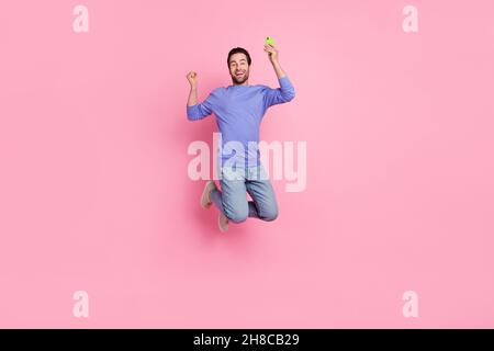 Full length photo of brunet cool millennial guy jump hold telephone wear blue pullover jeans sneakers isolated on pink background Stock Photo