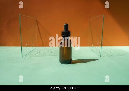 Front view of face serum amber bottle on dual background, pieces of glass with water drops as frame. Stock Photo