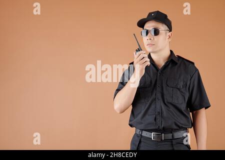 Portrait of serious security worker in black uniform using walkie-talkie Stock Photo