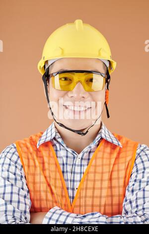 Smiling young construction site worker in hardhat and protective goggles looking at camera Stock Photo