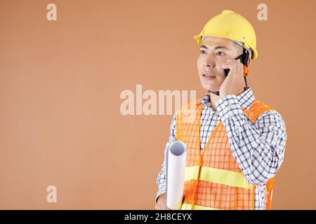 Construction engineer holding blueprint and talking on phone with client or colleague Stock Photo