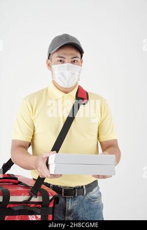 Portrait of handsome young courier in medical mask delivering hot pizza to customer Stock Photo
