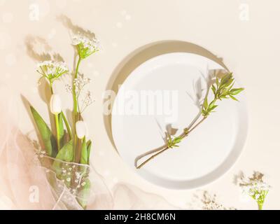Spring flower holiday composition with white tulips, gypsophila and green twig on a white plate on a pink background with shadows and bokeh effect. Fe Stock Photo