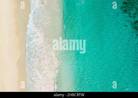 Aerial Top view of sand beach and blue sea. Aerial shot of beach meeting blue ocean water and foamy waves. Aerial beach top view overhead seaside. Stock Photo
