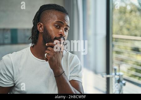 Man touching his beard with one hand before mirror Stock Photo
