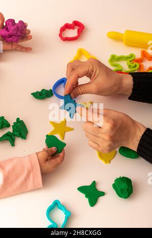 Girl playing dough with her mother. mother and daughter playing on a white background. Making various shapes with dough. Close-up. Mothers Day Stock Photo