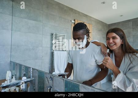 Smiling lady examining foam on male face standing before mirror Stock Photo