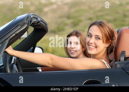 Two happy friends looking at you in a convertible car in the mountain Stock Photo