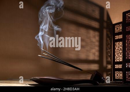 Smoke from burning incense sticks standing on lotus incense holder Stock Photo