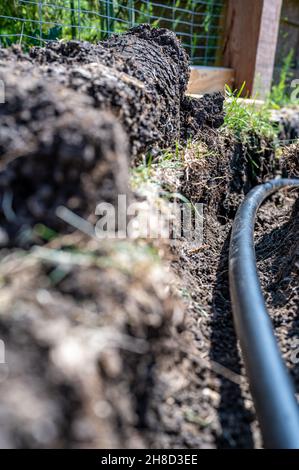 Focus on a black 1 inch sprinkler plastic water line laid in a shallow trench Stock Photo