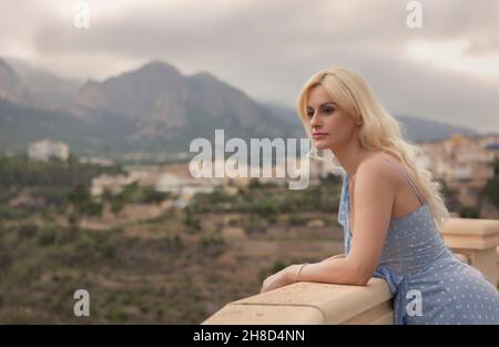 Woman in polka dot dress, leaning on the balcony railing with beautiful view Stock Photo