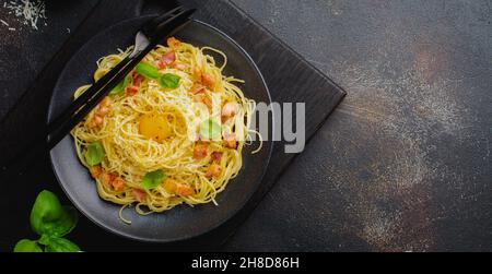 Pasta spaghetti carbonara with bacon, parmesan cheese, egg yolk and basil leaves on black background. Traditional Italian dish. Top view. Stock Photo