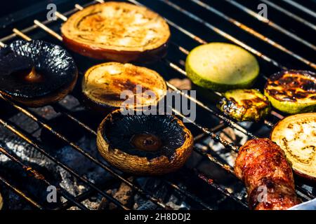 Grilling meat rolls called mici or mititei with vegetables on char barbecue. Charcoal grill with burning fire Stock Photo