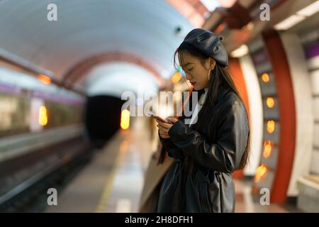 Chinese girl with smartphone at metro platform. Stylish female browsing social media wait for train Stock Photo