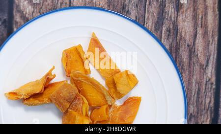 Dried orange mango on white and blue plate against wood background Stock Photo