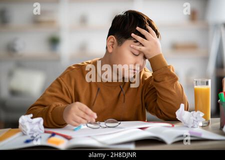 Exhautsed asian kid doing homework, experiencing difficulties, copy space Stock Photo