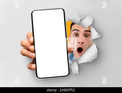 Shocked man showing white empty smartphone screen breaking through paper Stock Photo
