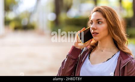Young natural girl talking with her smartphone in the park Stock Photo