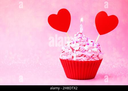 Valentines day cupcake. Cupcake with pink cream and sprinkled, with red heart and sparkler on a pink background with bokeh. Concept postcard to Valent Stock Photo