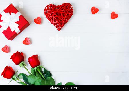 Kraft Gift box with beautiful white ribbon and red rose, candles in the form of a heart next to a red Kraft heart, on a white wooden background. Copy Stock Photo