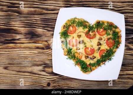 Valentines Day food. Heart shaped pizza with greens, on a white plate, on a wooden dark background. Top view. Copy space Stock Photo