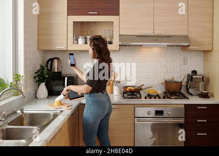 Financial analyst cutting vegetables for dinner and checking reports that colleague sent her Stock Photo