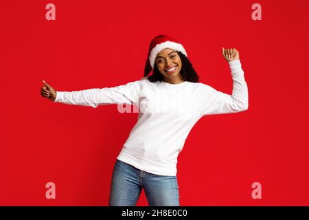 Positive black woman in Santa hat dancer moving on red Stock Photo