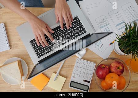 Hands of female ui designer typing on laptop and answering e-mals of client, view from above Stock Photo