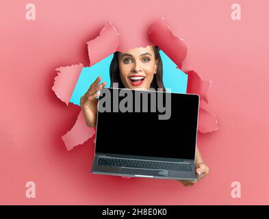 Young lady showing empty laptop screen through torn paper Stock Photo