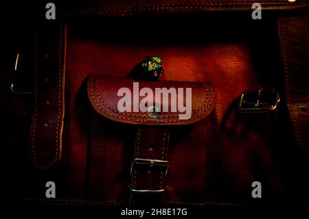 Dark Image of a green 20-sided die on a brown leather bag in warm light Stock Photo