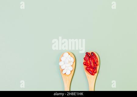 Pills and capsules in wooden spoons on green background with copy space, flat lay Stock Photo