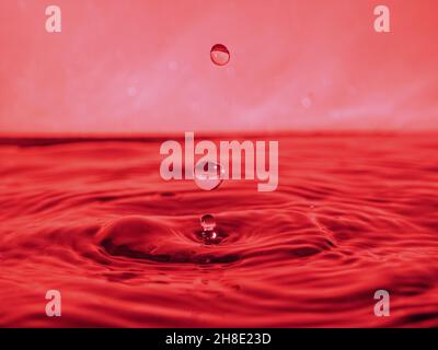 A red drop drips into the water and creates splashes of different shapes, due to the splashes waves are created on the water, the concept of a liquid Stock Photo