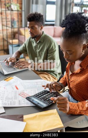 Focused young African American couple sitting at table with papers and analyzing costs while preparing documents to get tax refund Stock Photo