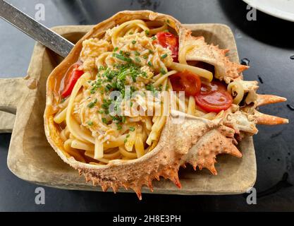 Fresh spider crab pasta served in its shell on wooden plate. Stock Photo