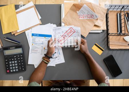 High angle view of unrecognizable blackman sitting at table with bills and checking arrears of payment Stock Photo