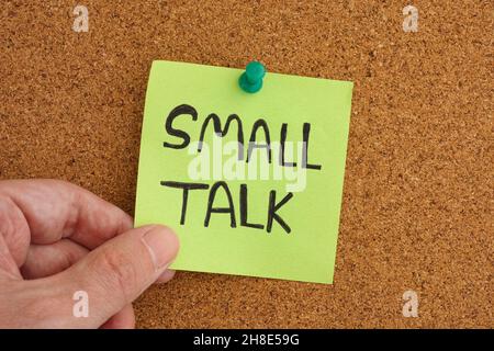 A man holding a sticky note that is pinned to a corkboard with the phrase Small Talk on it. Close up. Stock Photo