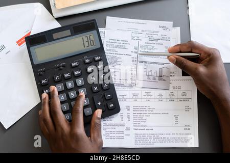 Above view of unrecognizable blackman checking receipts using calculator at table Stock Photo