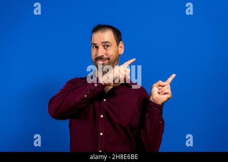 Handsome smiling bearded man pointing away on blue background. Stock Photo