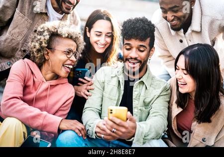 Multicultural friends having fun with mobile phone at campus college yard - Young men and women spending time together sharing funny video Stock Photo