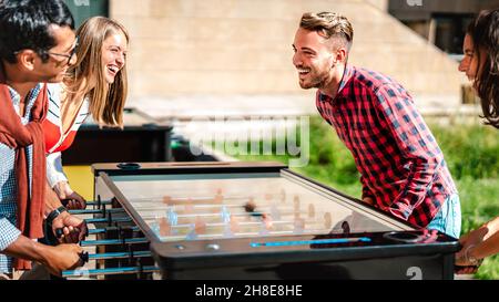 Multicultural friends play kicker table foosball at open space bar -Friendship life style concept with happy millennial having fun together at garden Stock Photo