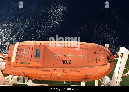 View from top on the orange colour life boat with reflective tape stickers secured with davits and safety hooks. Stock Photo