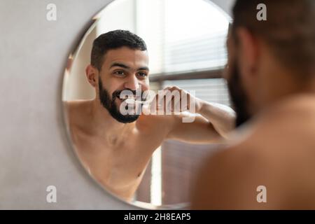 Handsome young Arab man using toothbrush in bathroom Stock Photo