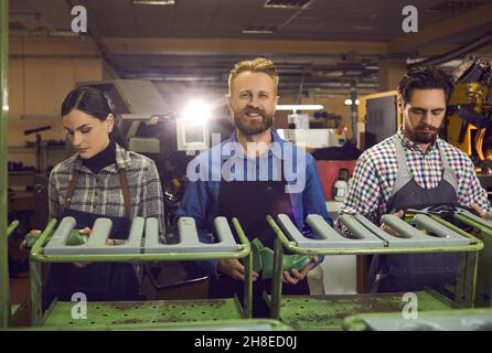 Three different shoe factory workers work together on the same machine in the workshop room. Stock Photo