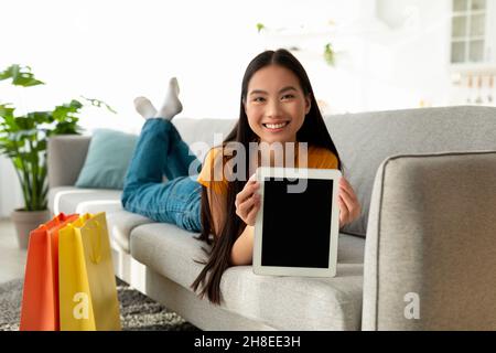 Online shopping concept. Happy asian lady holding digital tablet with blank screen, showing mockup for ad or design Stock Photo