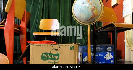 A school supply storeroom with chairs, a terrestrial globe, a box of Frito Lay snacks and photocopy paper; discarded school goods for later use. Stock Photo