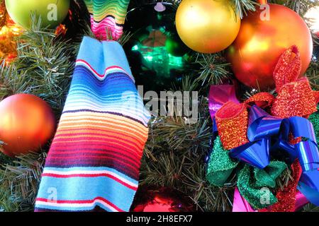 Hispanic-themed decorations on a Christmas tree; Mexican blanket, plastic ball orbs, ribbons; Holiday celebration in the United States Southwest. Stock Photo